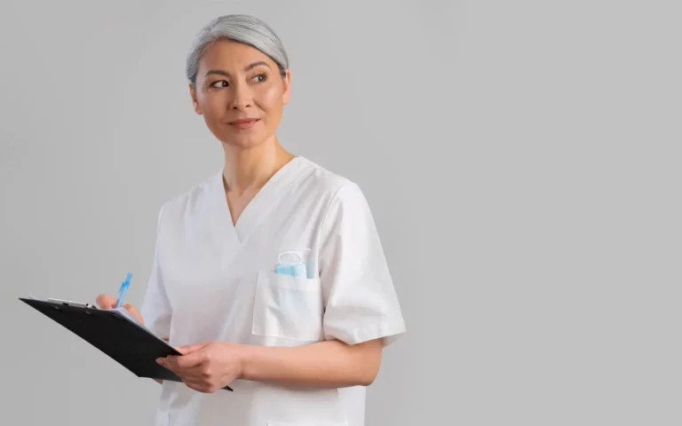 Mujer con bata y pelo blanco sujetando una carpeta sobre fondo blanco y representando a los mejores médicos estéticos